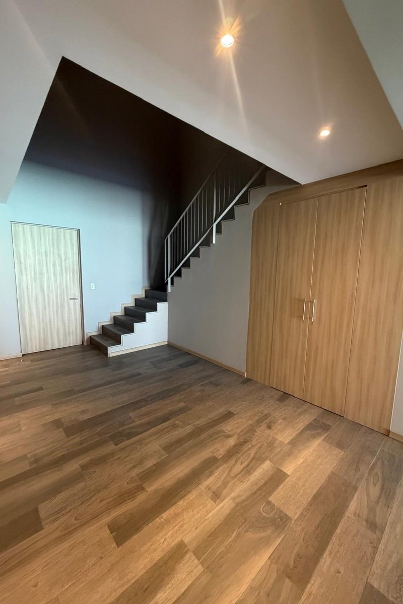 La escalera de madera entre el muro oscuro y la doble altura